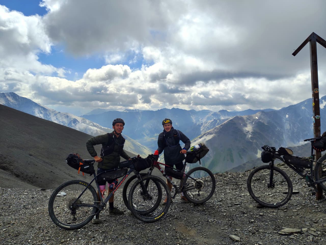 Two cyclists with loaded bikes at a high mountain pass in Georgia